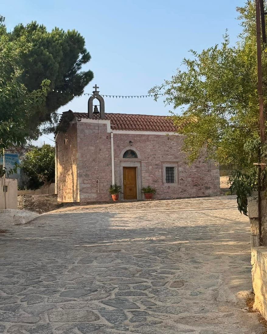 The stone church at the heart of Kounali, with its bell gable and tiled roof, on a cobbled street strung with colourful pennants