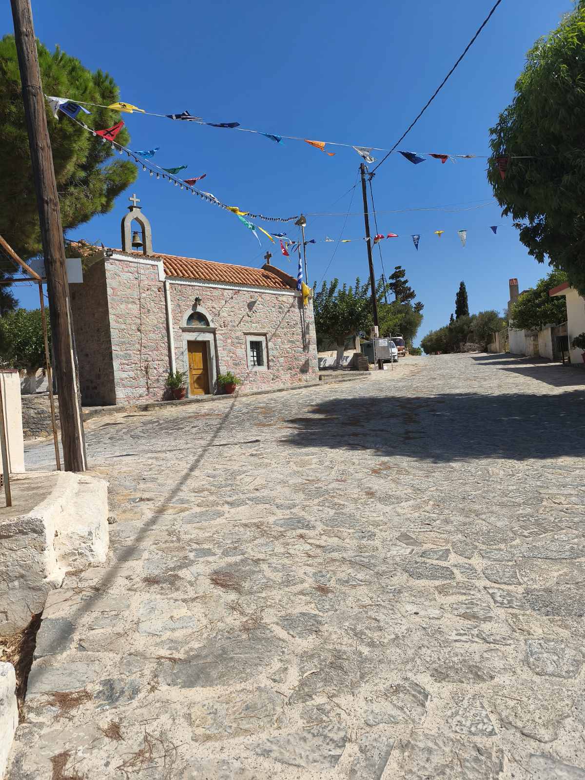 Η πέτρινη εκκλησία στην καρδιά του Κουναλιού, με το καμπαναριό και την κεραμοσκεπή της, σε πλακόστρωτο δρόμο στολισμένο με πολύχρωμα σημαιάκια