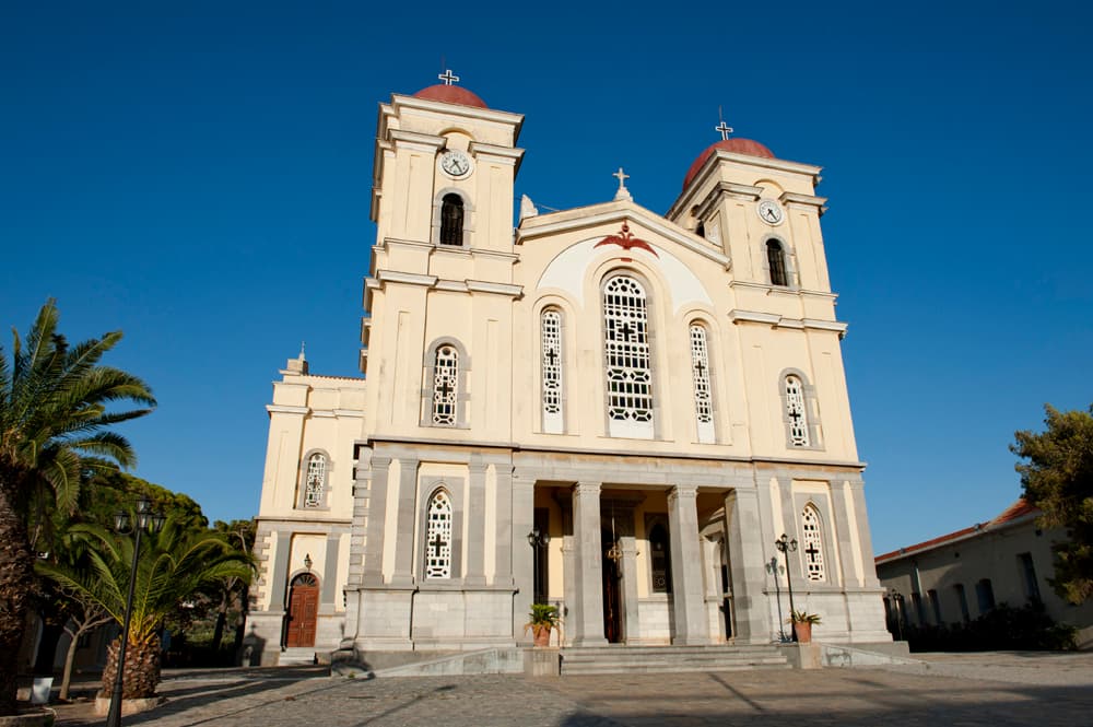 Ο ναός της Μεγάλης Παναγίας στην κεντρική πλατεία της Νεάπολης: δύο καμπαναριά με ρολόγια και κόκκινους τρούλους υψώνονται στον καταγάλανο ουρανό